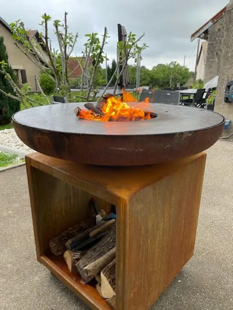 Brasero en acier corten allumé sur socle avec rangement bois dans l'Ain